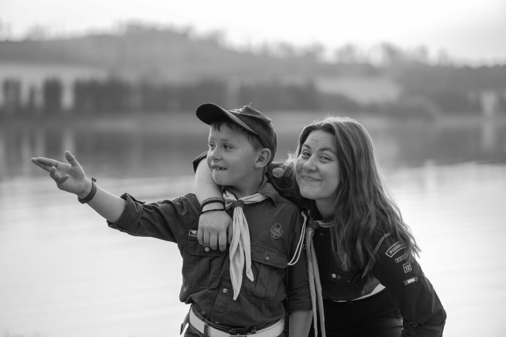 Dívka ukazuje směrem vzhůru, vedle ní chlapec – moment z dětského tábora nebo skautu.